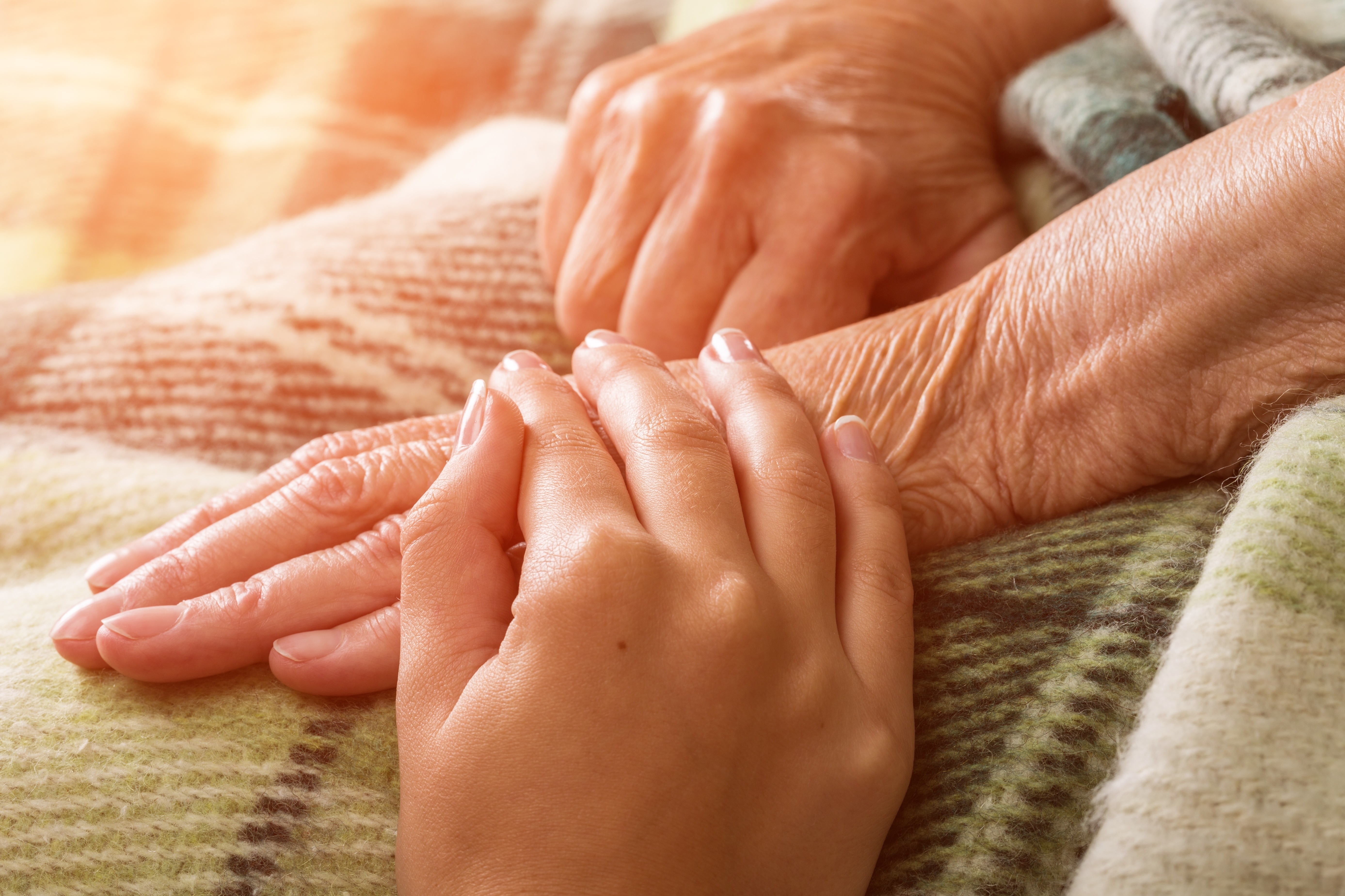 A caregiver holding an elderly patient's hand in home hospice care
